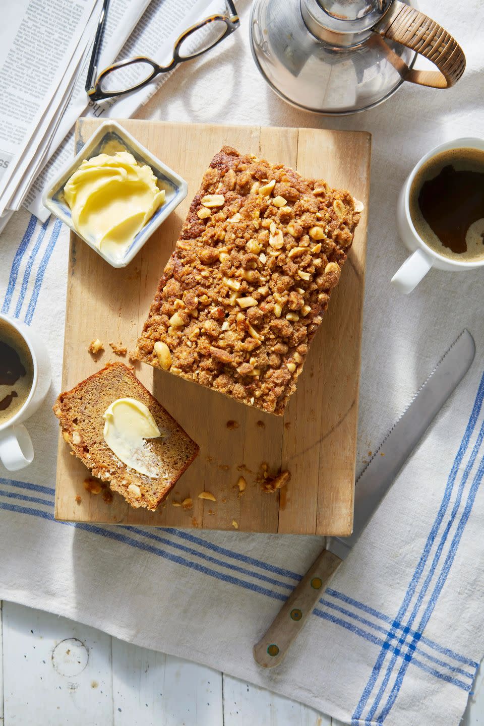 banana bread with salted peanut streusel on a cutting board with a cup of coffee