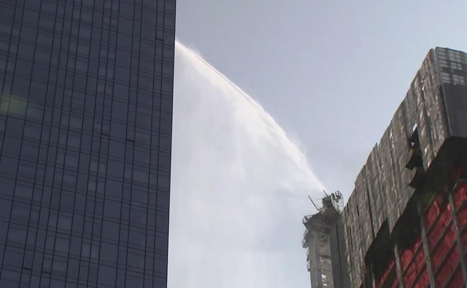 First responders spray water on tall construction crane that caught fire in Manhattan on Wednesday, July 26, 2023 in New York. The crane caught fire and its arm hit a building as it crashed to the street below. (WABC via AP)