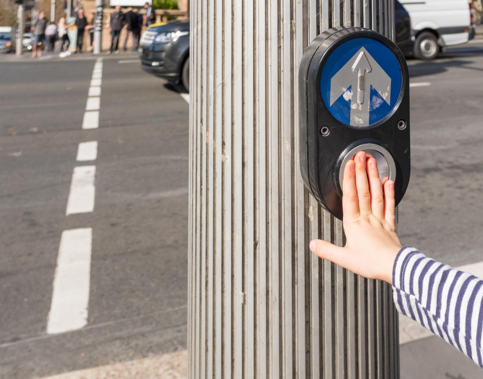 Cropped view of child's hand pushing an Australian pedestrian crossing button (selective focus)