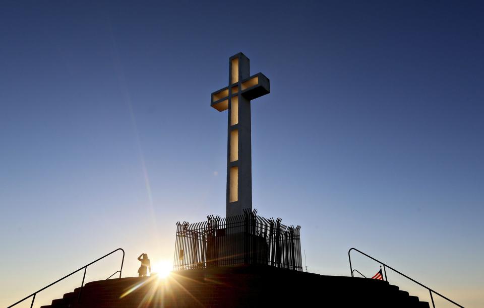 People gather in the late evening sun around the massive cross sitting atop the Mt. Soledad War Memorial in La Jolla