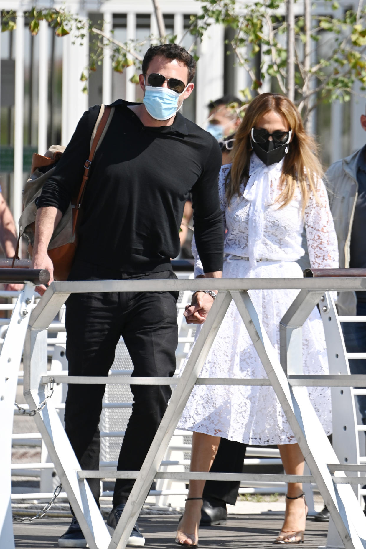 Ben Affleck, dressed in an all-black outfit, holds hands with Jennifer Lopez, wearing a Valentino lace shirt dress, as the pair arrive at the 78th Venice International Film Festival on September 09, 2021 in Venice, Italy. (Getty Images)