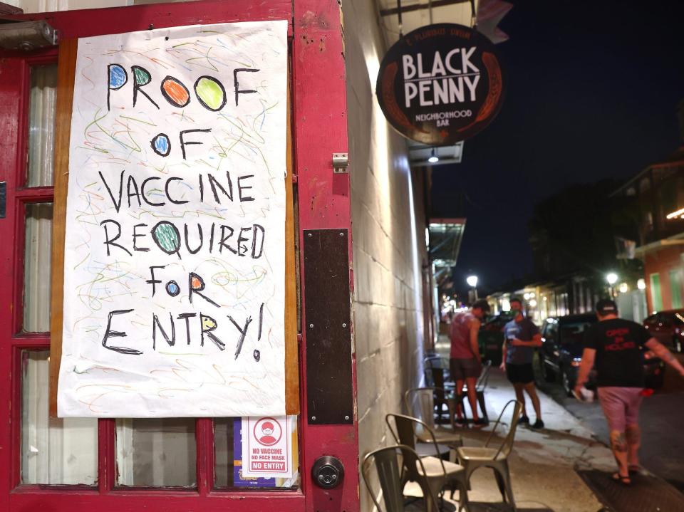 A sign hung on a bar door reads 'Proof of vaccine required for entry!' on a busy street at night