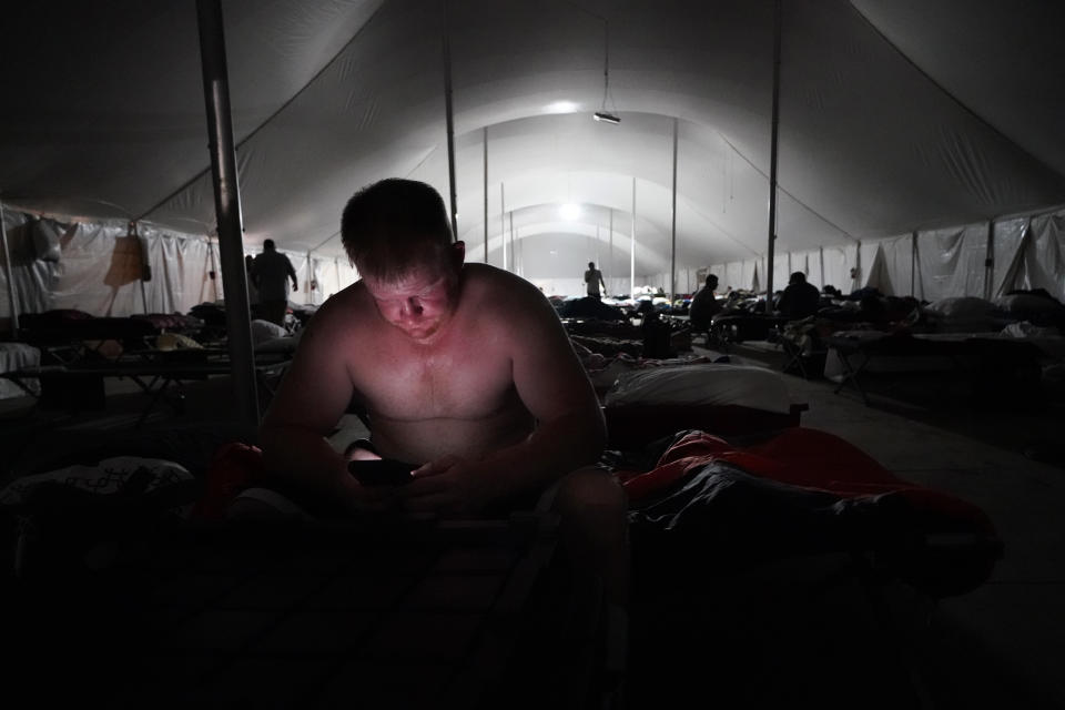 Bryan Willis, of Stilwell, Okla., an electrical worker for Ozarks Electric, looks at his phone before going to bed in a tent city for electrical workers in Amelia, La., Thursday, Sept. 16, 2021. When Hurricane Ida was brewing in the Gulf of Mexico, the grass was chest high and the warehouse empty at this lot in southeastern Louisiana. Within days, electric officials transformed it into a bustling “tent city” with enormous, air-conditioned tents for workers, a gravel parking lot for bucket trucks and a station to resupply crews restoring power to the region. (AP Photo/Gerald Herbert)