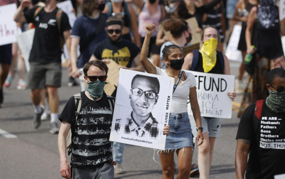 Demonstrators carry placards as they walk down Sable Boulevard during a rally and march over the death of 23-year-old Elijah McClain, Saturday, June 27, 2020, in Aurora, Colo. McClain died in late August 2019 after he was stopped while walking to his apartment by three Aurora Police Department officers. (AP Photo/David Zalubowski)