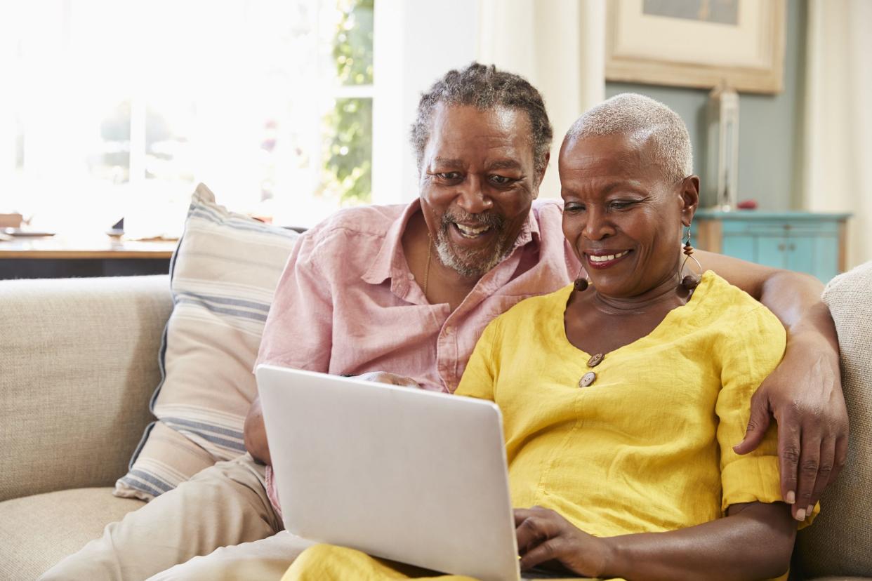 senior couple sitting on sofa using laptop at home together