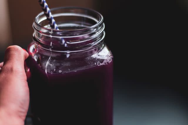 <p>Malorny / Getty Images</p> Hand holding glass of prune juice