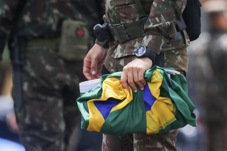 A soldier carefully collects national flags after supporters of former Brazilian former President Jair Bolsonaro left the encampment set up outside army headquarters in Brasilia, Brazil, Monday, Jan. 9, 2023, the day after Bolsonaro supporters stormed government buildings in the capital. (AP Photo/Gustavo Moreno)