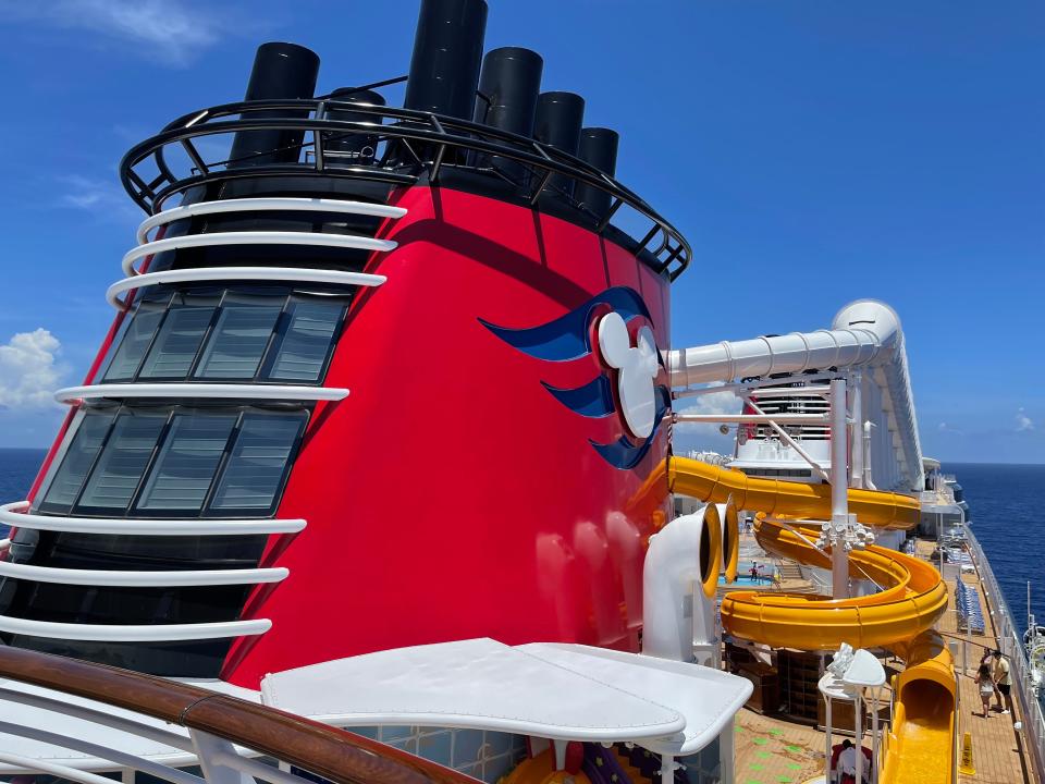 The exterior of the Disney Wish cruise ship, which shows a red wall with a Mickey Mouse symbol and white and yellow waterslides.
