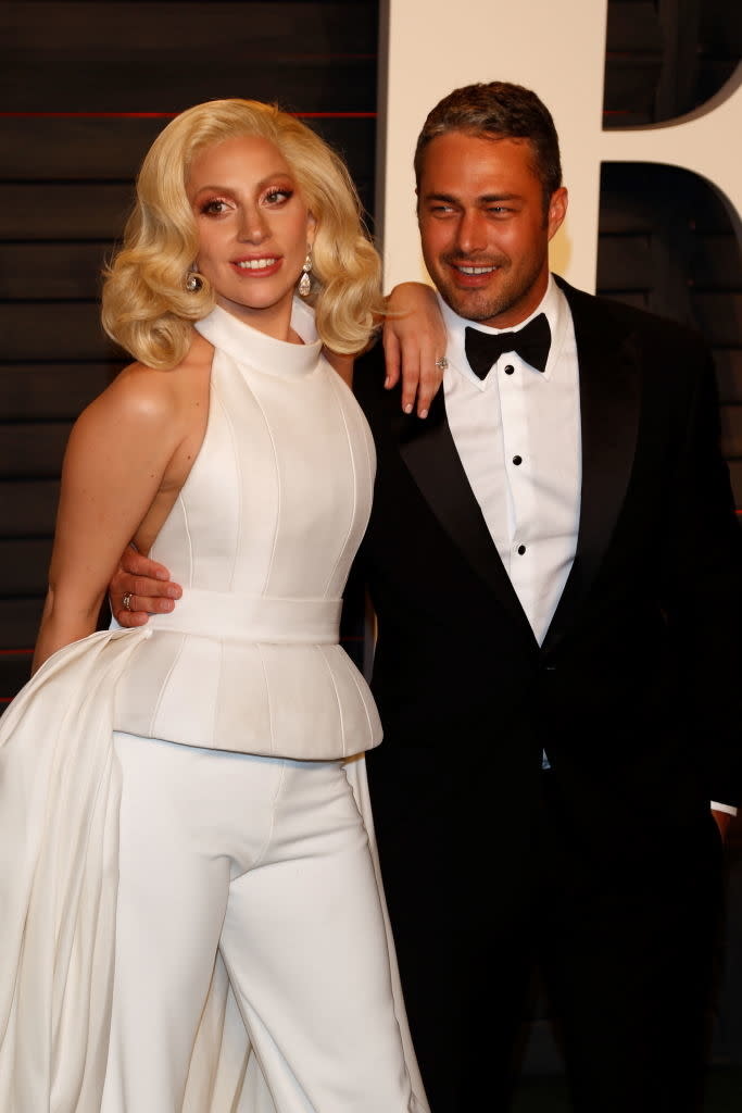 Lady Gaga in a gown with pants with Taylor Kinney in a tuxedo at an event