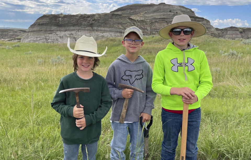 In this image provided by Giant Screen Films, Liam Fisher, Kaiden Madsen and Jessin Fisher pose for a celebratory photo on the day their fossil find was determined to be a juvenile T. rex, in North Dakota. A documentary film crew captured the moment of discovery for the film "T.REX." (David Clark/Giant Screen Films via AP)