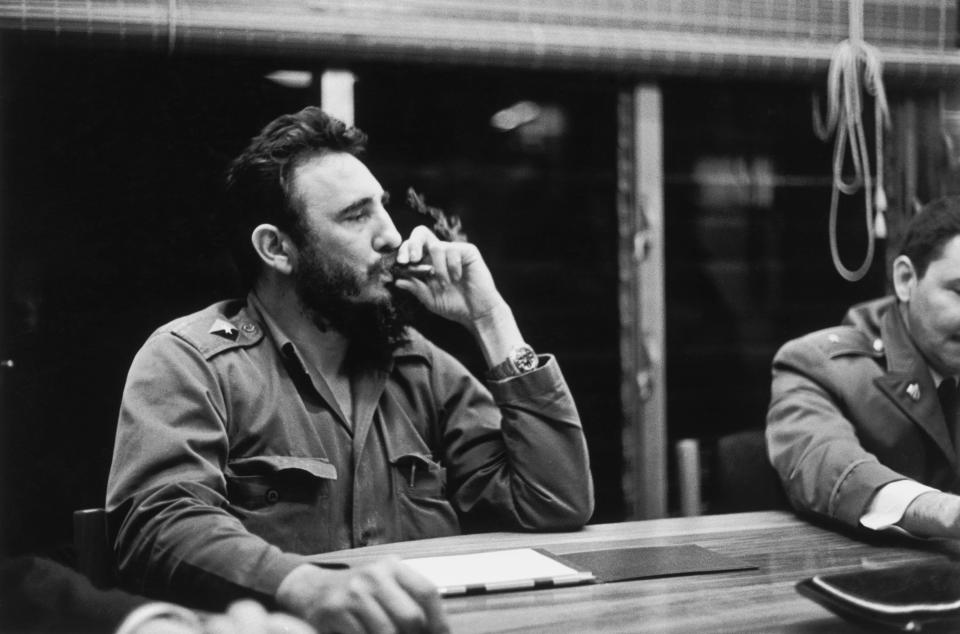 A photo of Fidel Castro sitting in a meeting and taking a drag of his cigar.
