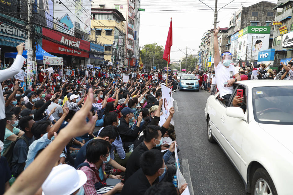 Protesters, seated on a road, flash the three-fingered salute as vehicles are driven past in Yangon, Myanmar, on Feb. 6, 2021. Protests in Myanmar against the military coup that removed Aung San Suu Kyi’s government from power have grown in recent days despite official efforts to make organizing them difficult or even illegal. (AP Photo)
