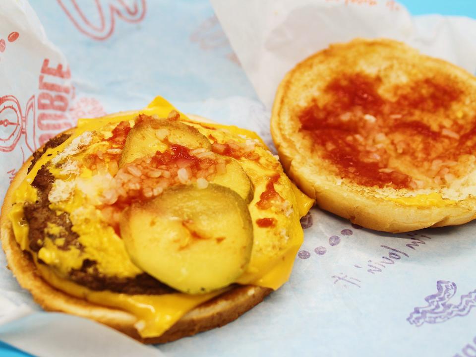 An opened-up mcdonalds double cheeseburger reveals ketchup, two pickles, onions and cheese on top of two patties.