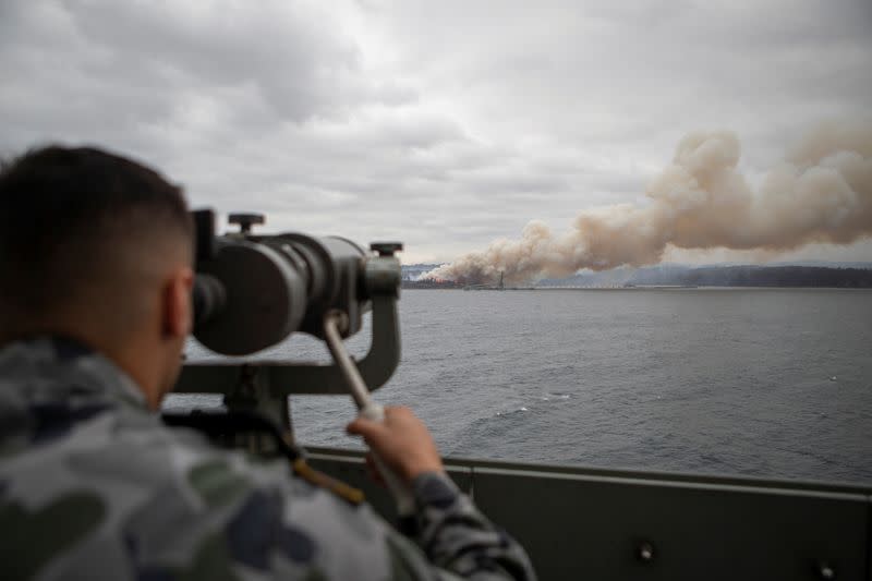 Seaman Boatswains Mate Malik El-Leissy views a burning fire from HMAS Adelaide as the ship arrives at Eden