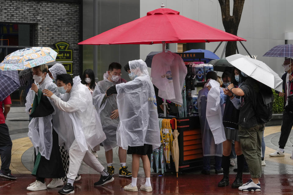 Visitors wearing face masks to help protect themselves from the coronavirus purchase raincoats from a store at the Universal Studios Beijing in Beijing, Monday, Sept. 20, 2021. Thousands of people brave the rain visit to the newest location of the global brand of theme parks which officially opens on Monday. (AP Photo/Andy Wong)