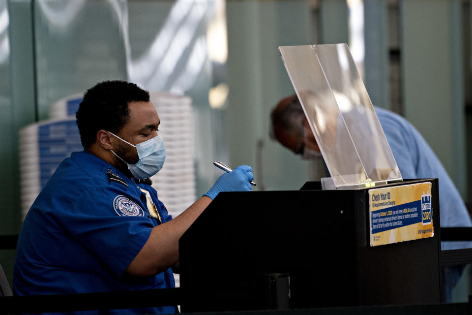 A Transportation Security Administration (TSA) agent wears a protective mask and sits behind a protective barrier while screening a traveler at Ronald Reagan National Airport (DCA) in Arlington, Virginia, U.S., on Tuesday, June 9, 2020. (Andrew Harrer/Bloomberg via Getty Images)