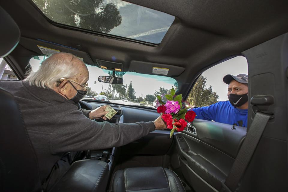 A man in a car reaches out to take flowers from a roadside vendor at his passenger's side window