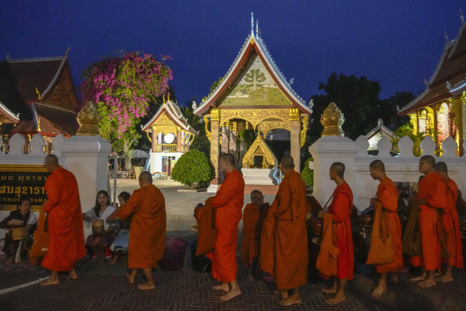 People offer food to Buddhist monks outside Sensoukharam temple in Luang Prabang, Laos, Sunday, Jan. 28, 2024. Luang Prabang was named a UNESCO World Heritage Site nearly 30 years ago, but a multibillion-dollar dam project is raising questions that could deprive the city of its coveted status and prompting broader concerns the Mekong River could be ruined by multiple dams that are being planned.(AP Photo/Sakchai Lalit)