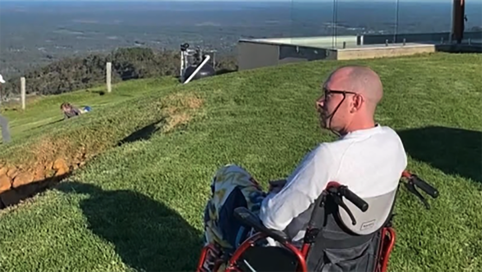 Lachlan Webb sitting in a wheelchair on a green hill after being diagnosed.