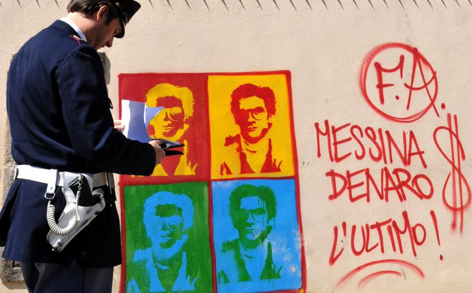 An Italian Police officer in Palermo, Sicily, looks on at graffiti on the perimeter wall of the city's cathedral, portraying Matteo Messina Denaro, a fugitive Mafia boss from the city of Trapani, in western Sicily - Alessandro Fucarini/AP