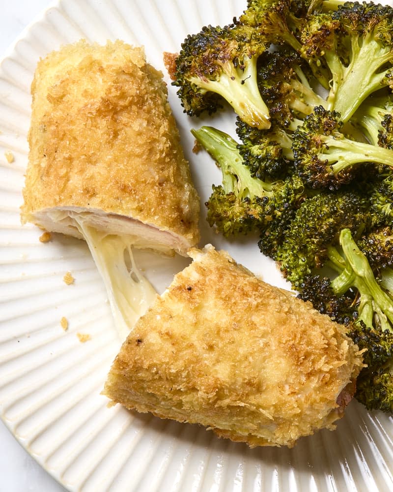 overhead shot of chicken cordon bleu sliced on a white scalloped plate with roasted broccoli.