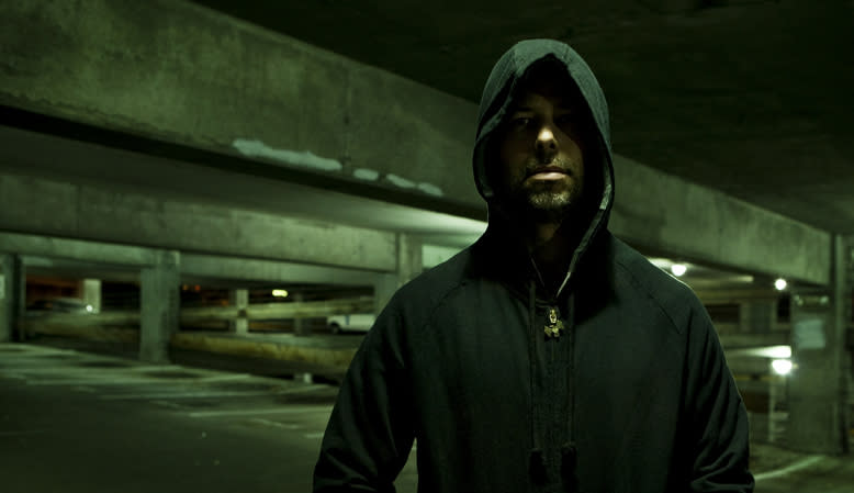 A person wearing a hooded jacket stands in a dimly lit parking garage