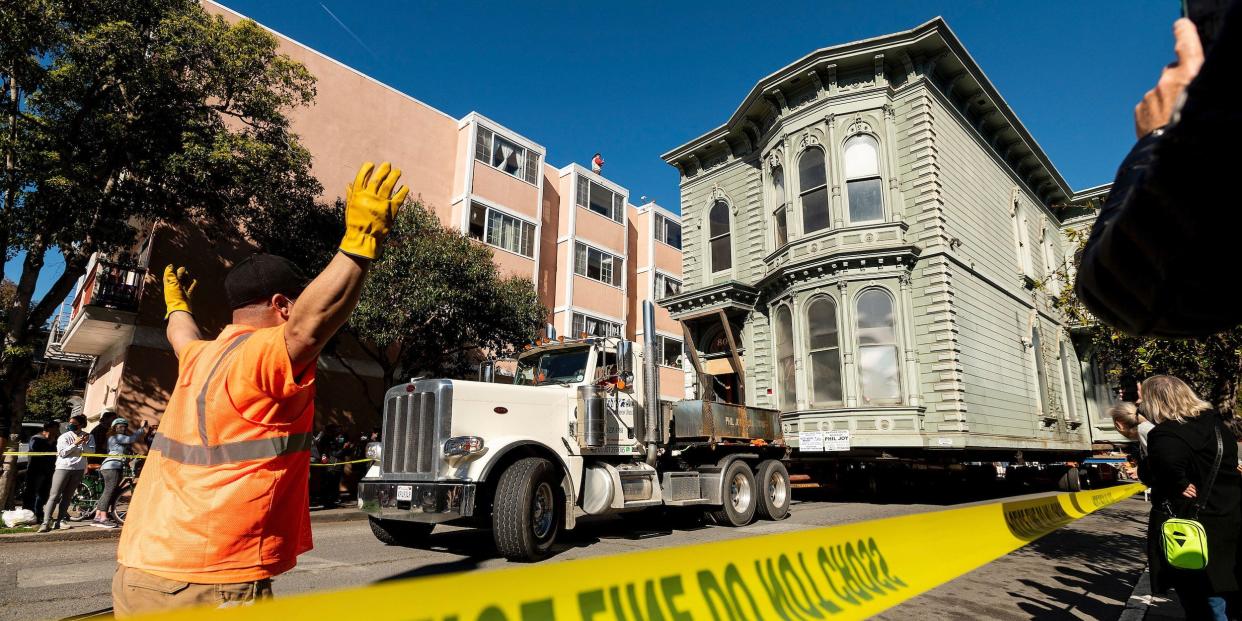 A worker signals to a truck driver pulling a Victorian home through San Francisco on Sunday, Feb. 21, 2021. The house, built in 1882, was moved to a new location about six blocks away to make room for a condominium development. According to the consultant overseeing the project, the move cost approximately $400,000 and involved removing street lights, parking meters, and utility lines.