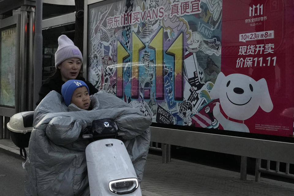 A woman and a child ride past an advertisement for Singles' Day in Beijing, Wednesday, Nov. 8, 2023. Shoppers in China have been tightening their purse strings, raising questions over how faltering consumer confidence may affect the annual Singles' Day online retail extravaganza. (AP Photo/Ng Han Guan)