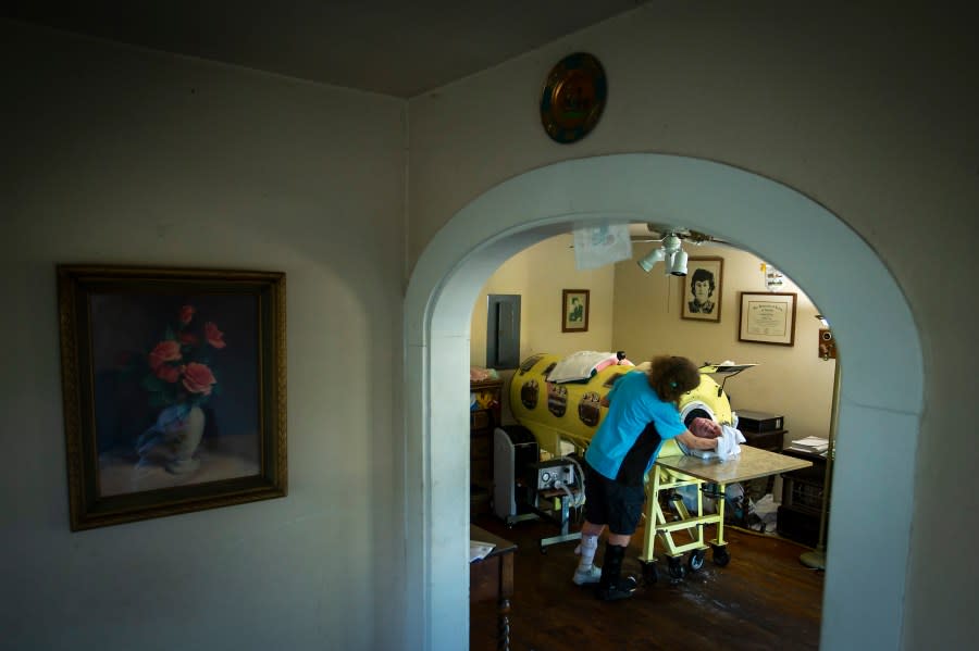 FILE – In this Friday, April 27, 2018 photo, caregiver and friend Kathryn Gaines washes the face of attorney Paul Alexander beside his iron lung at his home in Dallas. Alexander died Monday, March 11, 2024 at a Dallas hospital, said Daniel Spinks, a longtime friend. He said Alexander had recently been hospitalized after being diagnosed with COVID-19 but did not know the cause of death. (Smiley N. Pool/The Dallas Morning News via AP)