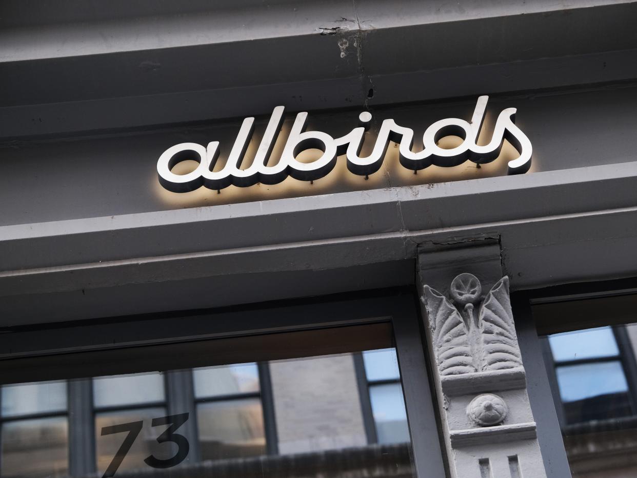 A neon Allbirds sign on the side of a grey building.