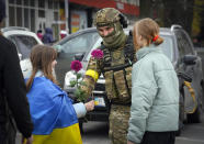 A girl wrapped in the national flag exchange flowers with a Ukrainian soldier in central Kherson, Ukraine, Sunday, Nov. 13, 2022. The Russian retreat from Kherson marked a triumphant milestone in Ukraine's pushback against Moscow's invasion almost nine months ago. (AP Photo/Efrem Lukatsky)