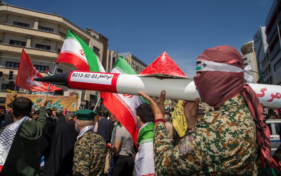 A man in army fatigues and with a face covering holds an replica missile.