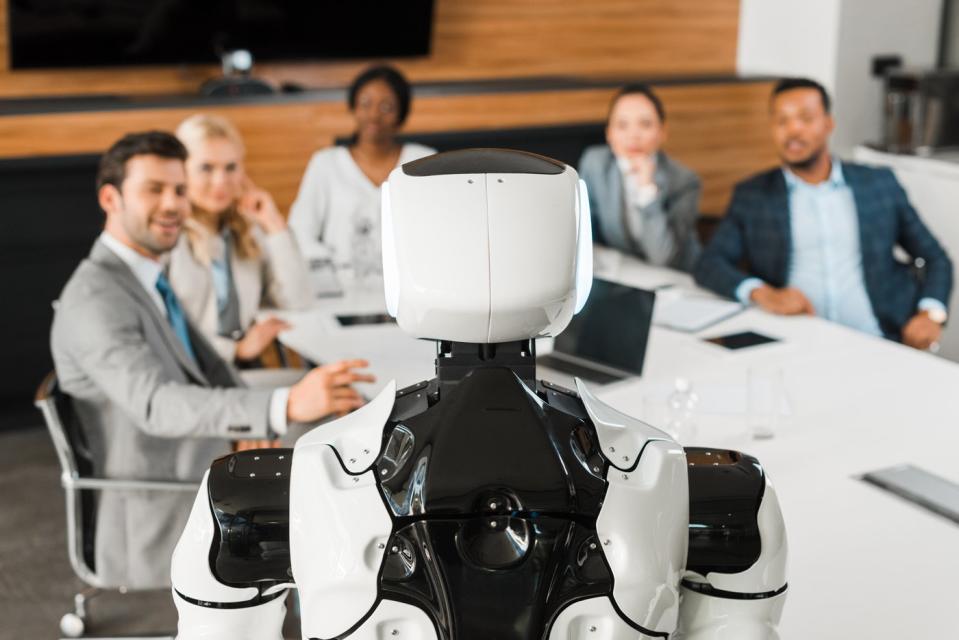 Human-like robot engaging with company employees around an office table. 