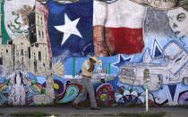 A man adjusts his face mask as he walks past a mural in the heavily Latino section of Oak Cliff in Dallas, Wednesday, Sept. 22, 2021. Texas this week will begin redrawing congressional lines, and Latino advocates and officeholders say it's time to correct past wrongs. The state's explosive population growth over the past decade, half of which comes from Latinos, has earned it two new congressional seats. At least one should be a Latino-majority congressional seat in the Dallas area, they argue. (AP Photo/LM Otero)