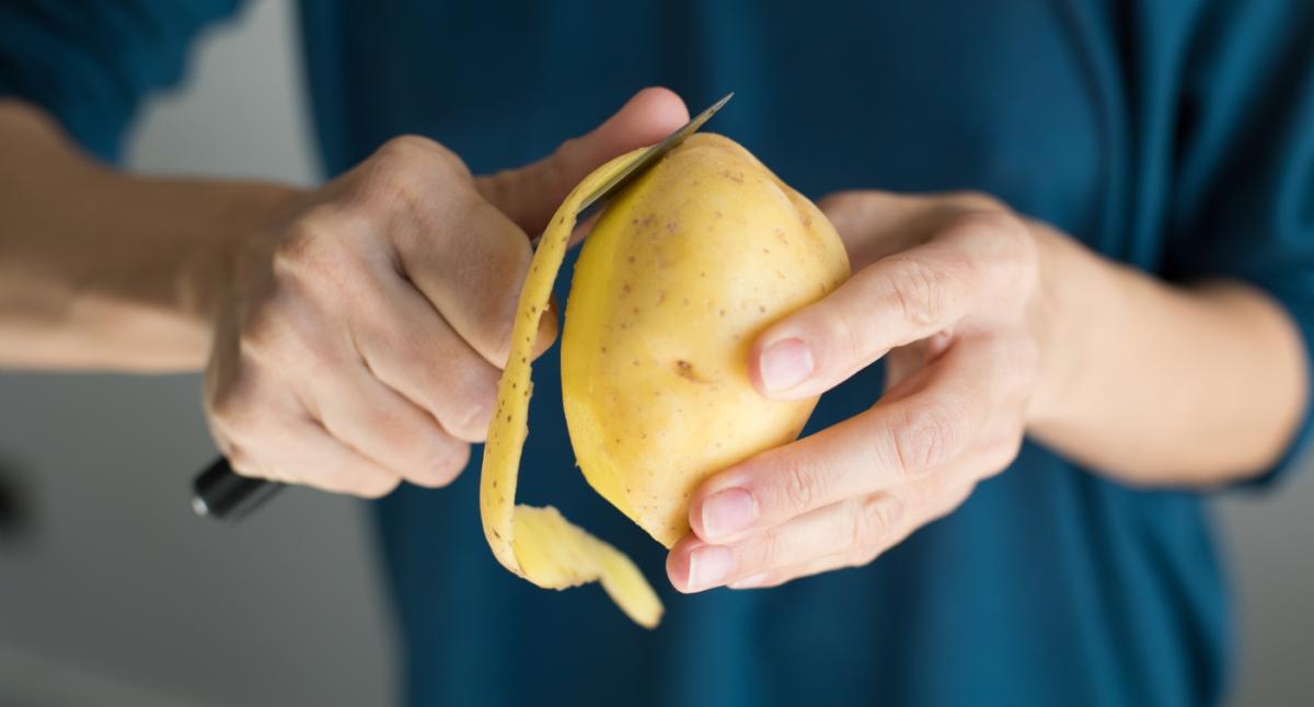 Boy using peeler to peel raw potato available as Framed Prints