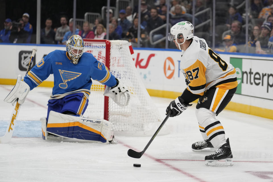 Pittsburgh Penguins' Sidney Crosby (87) controls the puck as St. Louis Blues goaltender Jordan Binnington (50) defends during the third period of an NHL hockey game Saturday, Oct. 21, 2023, in St. Louis. (AP Photo/Jeff Roberson)