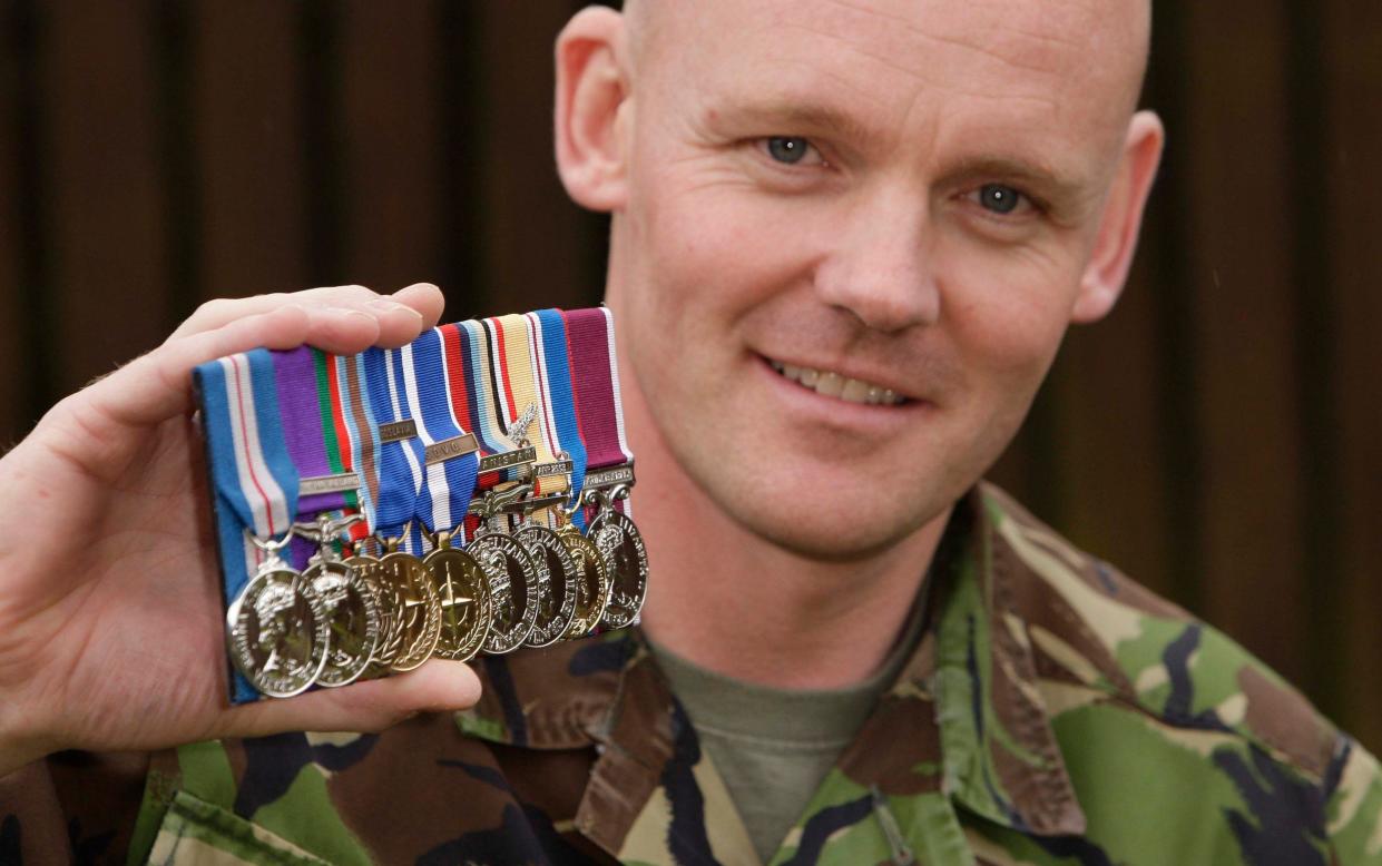 Maj Owers holds up his medals, including the Queen's Gallantry award, while wearing camouflage gear