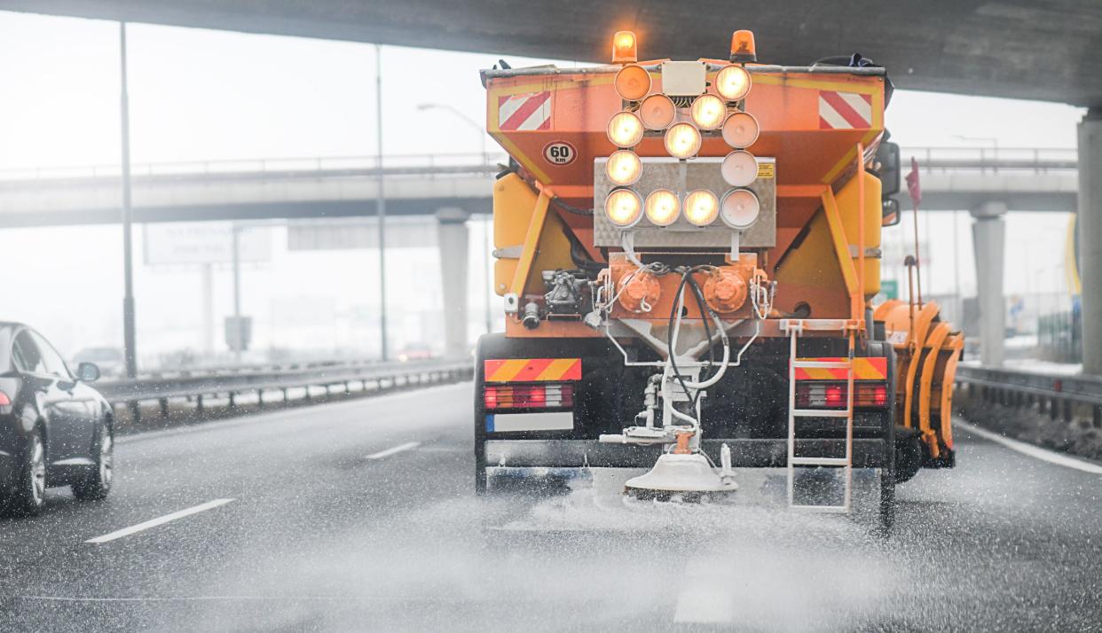 Snow plow salting street in winter time. Orange truck deicing. Maintenance winter vehicle back side.