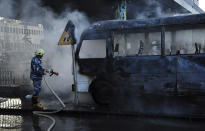 In this photo released by the Syrian official news agency SANA, a Syrian firefighter extinguishes a burned bus at the site of a deadly explosion, in Damascus, Syria, Wednesday, Oct. 20, 2021. Two roadside bombs exploded near a bus carrying troops during the morning rush hour in the Syrian capital early Wednesday, killing and wounding several people, state TV reported. (SANA via AP)