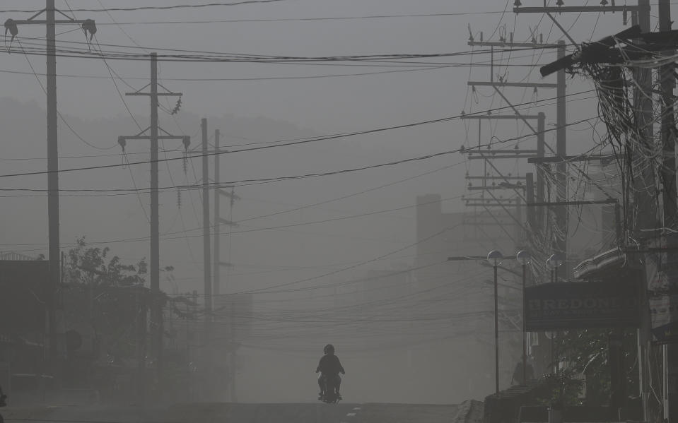 Un motociclista pasa por una calle mientras el viento levanta ceniza del volcán Taal en Lemery, un pueblo evacuado en la provincia de Batangas, en el sur de Filipinas, el jueves 16 de enero de 2020. (AP Foto/Aaron Favila)