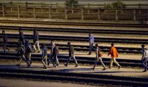 Migrants walk along railway tracks at the Eurotunnel terminal on July 28, 2015 near Calais