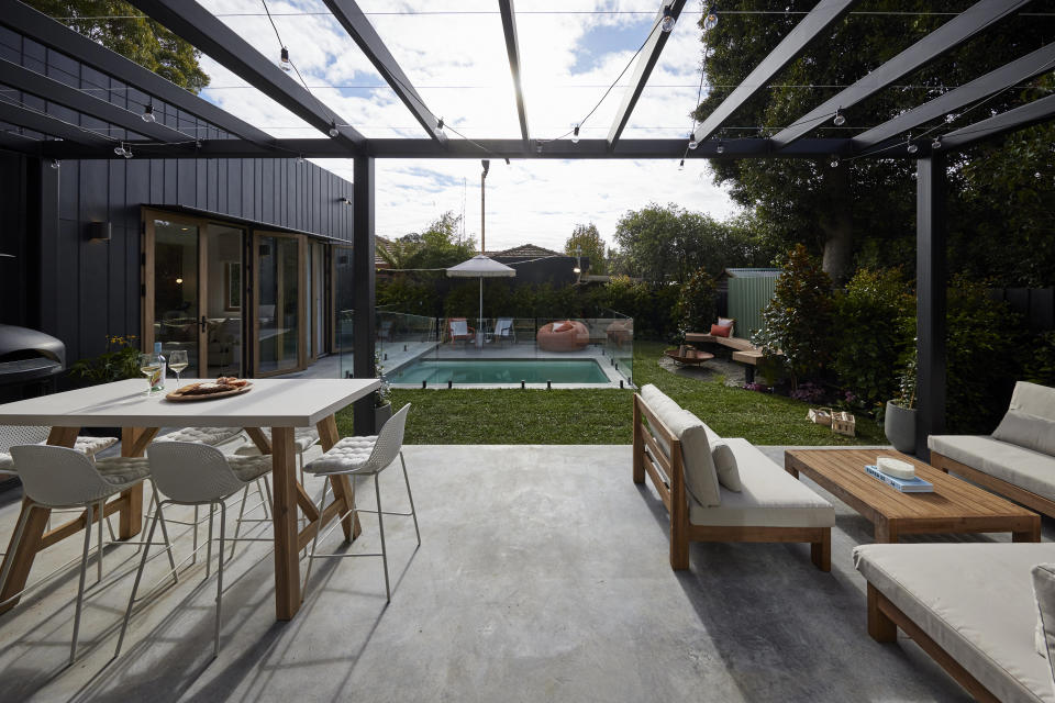 The concrete area with a table and chairs and lounges, opening out to the rest of the backyard. 