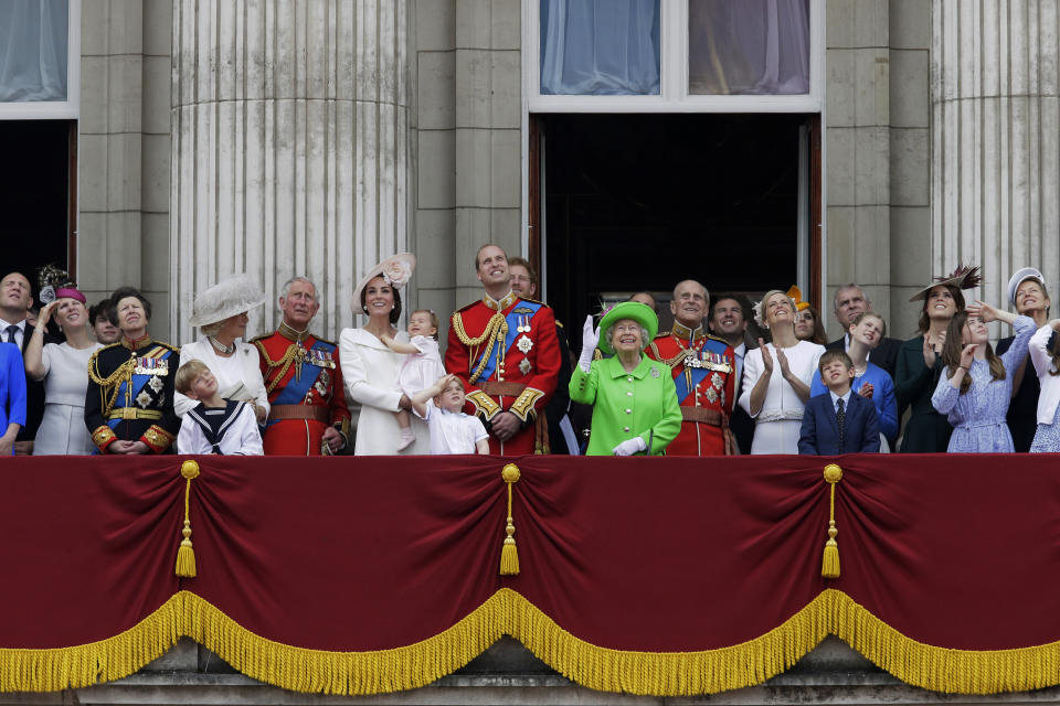 FILE - In this June 11, 2016 file photo, Britain's Queen Elizabeth II waves as she watches the flypast, with Prince Philip, to right, Prince William, centre, with his son Prince George, front, Kate, Duchess of Cambridge holding Princess Charlotte, centre left, with The Prince of Wales standing with The Duchess of Cornwall, and Princess Anne, fourth left, on the balcony during the Trooping The Colour parade at Buckingham Palace, in London. The timing couldn’t be worse for Harry and Meghan. The Duke and Duchess of Sussex will finally get the chance to tell the story behind their departure from royal duties directly to the public on Sunday, March 7, 2021 when their two-hour interview with Oprah Winfrey is broadcast. (AP Photo/Tim Ireland, File)