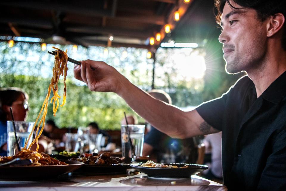 A man pulling noodles from a steaming bowl at a restaurant.