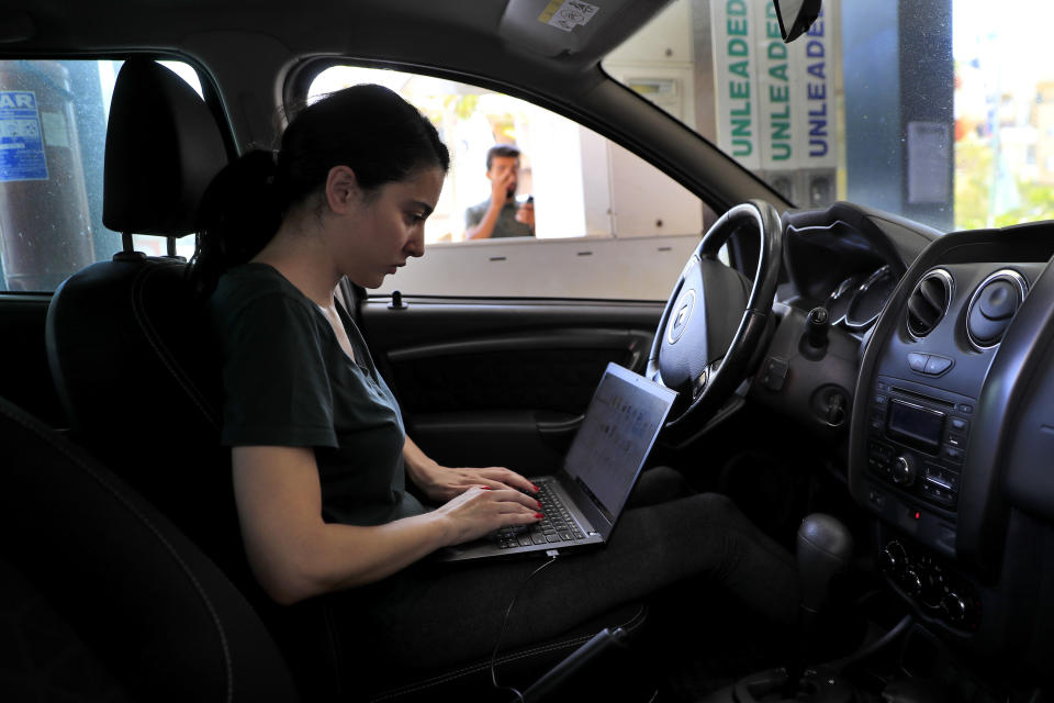 An employee saves time by working on her laptop while waiting on a long queue to fill her car with gasoline in Beirut, Lebanon, Friday, June 25, 2021. Lebanon's caretaker prime minister on Friday granted his approval to allow the financing of fuel imports at a rate higher than the official exchange rate, effectively reducing critical fuel subsidies that have been in place for decades, amid worsening gasoline shortages. (AP Photo/Hussein Malla)