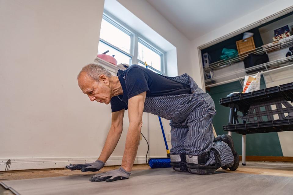 Senior man wearing overalls, laying wood flooring.