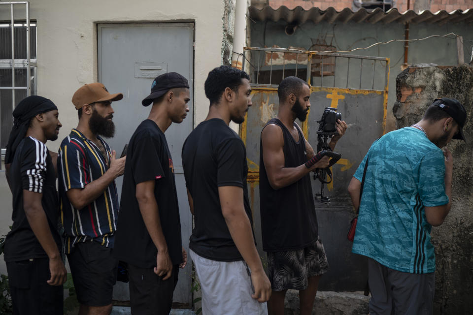 Producer Giovani Rafael, second left, directs Trap de Cria artist Ramon Silva, known as "Suav," right, as cameraman Gabriel Santana "San" records a music video in the Parada de Lucas slum of Rio de Janeiro, Brazil, Sunday, April 4, 2021. Trap de Cria has a lyrical flow over synthesized drums, and is comparable to U.S. gangsta rap in speaking to the day-to-day struggles of hardscrabble hoods while depicting gang life. (AP Photo/Felipe Dana)