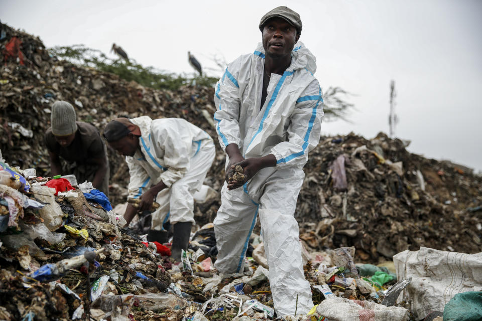 Duncan Wanjohi, right, and Kelvin Kimani, center, scavenge for recyclable materials on Sunday, March 28, 2021, from Dandora, the largest garbage dump in Kenya's capital of Nairobi. Their protective medical suits were found among material thrown away from hospitals. An estimated 20 million people around the world help keep cities clean by scavenging through landfills and dumps. Experts say these trash pickers, who sometimes toil alongside paid municipal sanitation workers, provide a vital service, yet they usually are not on a priority list for coronavirus vaccines. (AP Photo/Brian Inganga)