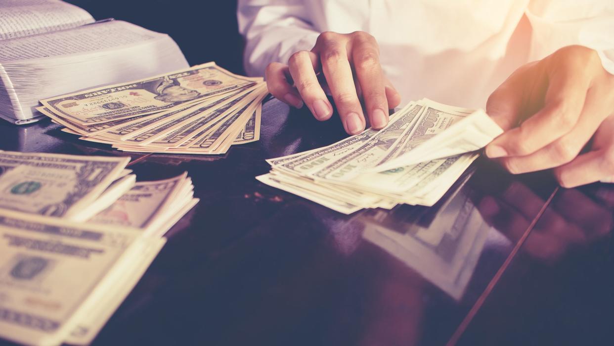 Bank teller's hands counting dollar banknotes on the table.