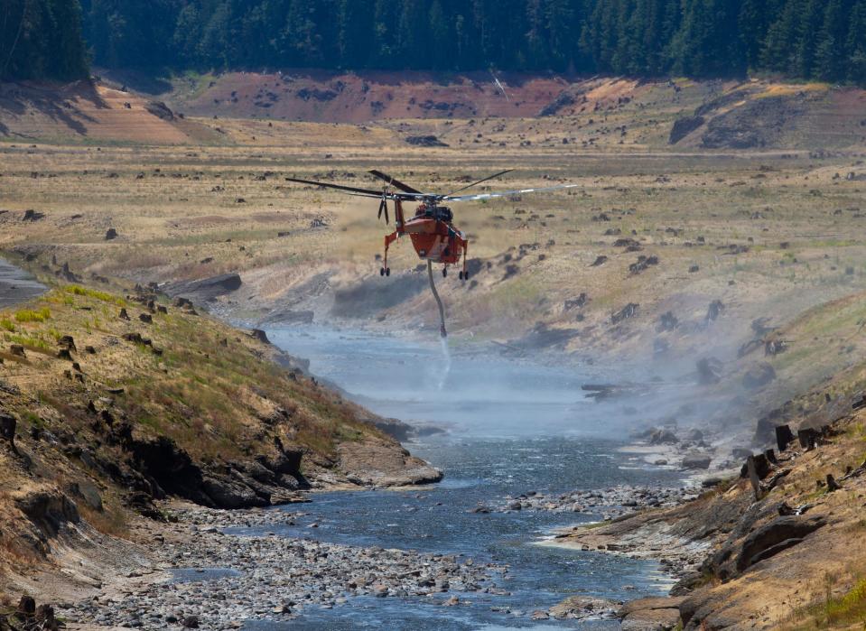 A helicopter squeezes between the banks of Fall Creek to get a load of water to battle the Bedrock Fire east of Eugene Monday, July 24, 2023.